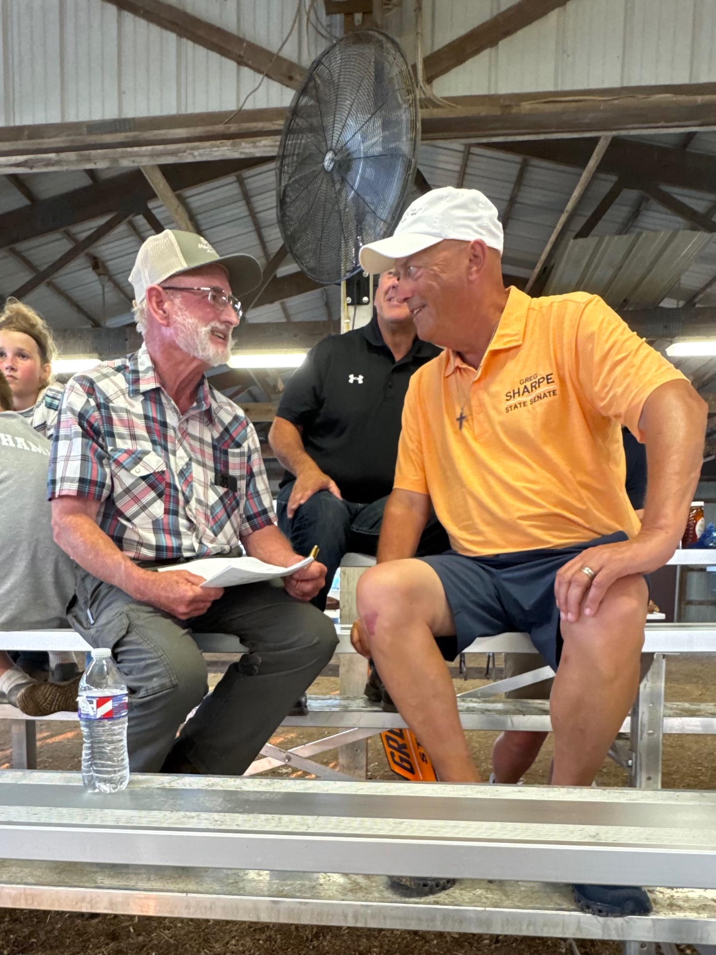 Greg Sharpe in his orange State Senate polo talking with a Northeast Missouri farmer on the bleachers at a county fair